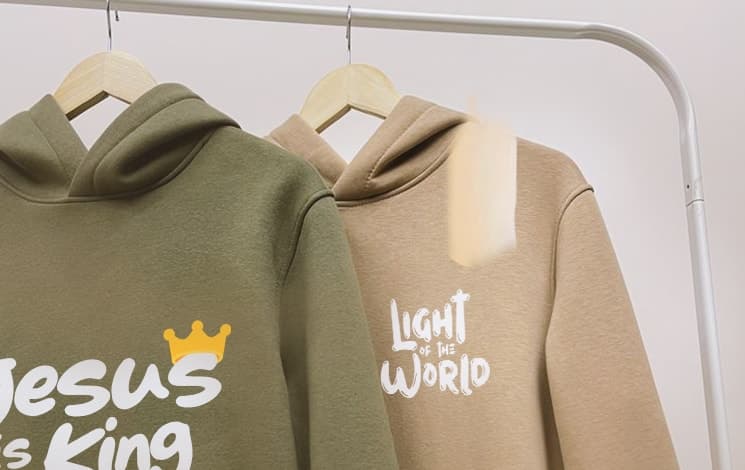 Olive “Jesus Is King” and sand “Light of the World” ADULLAM hoodies on hangers.